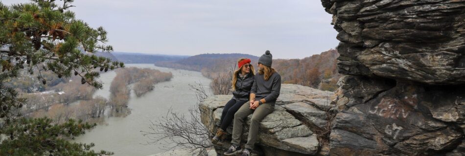 Couple sitting on a rock overlooking Harpers Ferry at the summit of Maryland Heights Overlook hiking trail